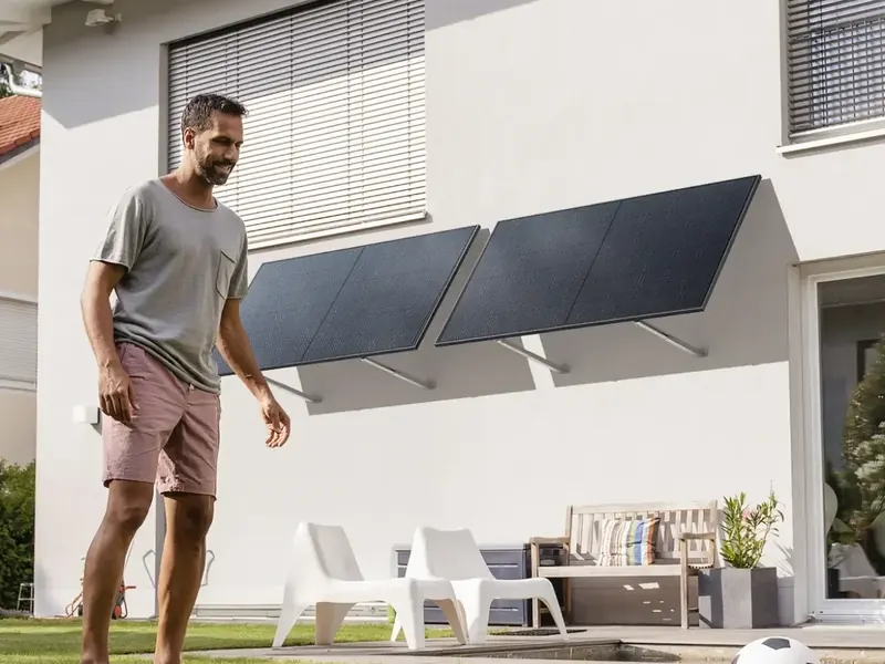 Solarmodule an verstellbaren Fassadenhalterungen an einer hellen Hauswand, davor ein Mann mit Fußball im Garten